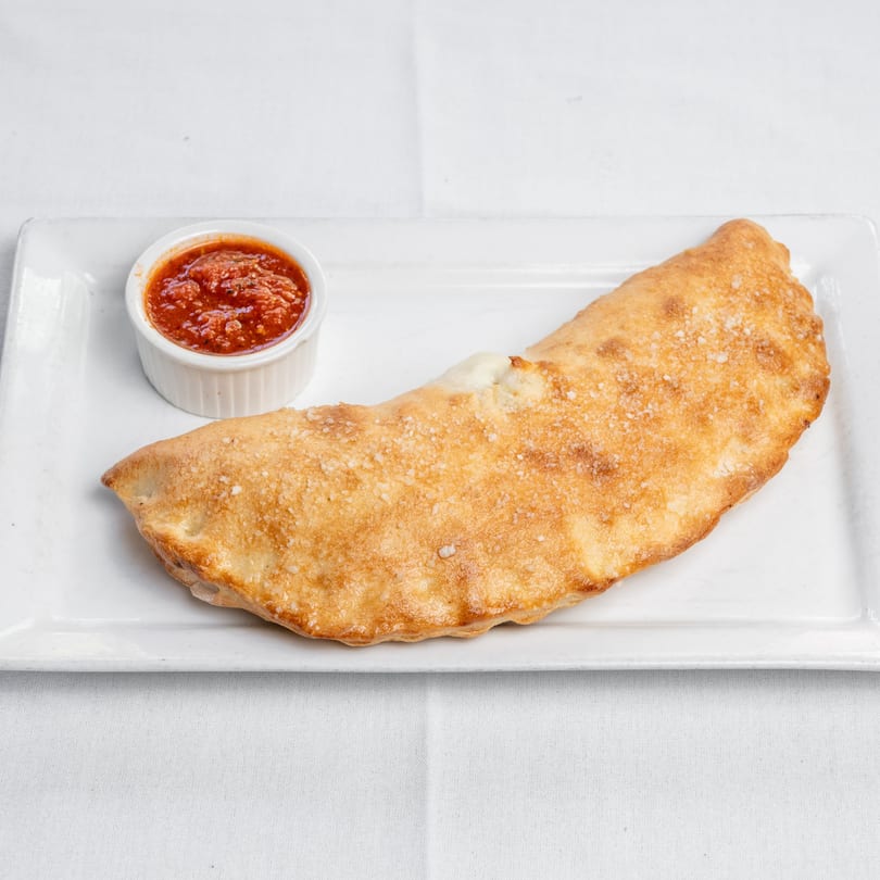 A golden-brown calzone with visible cheese and a side of red marinara sauce on a white plate.